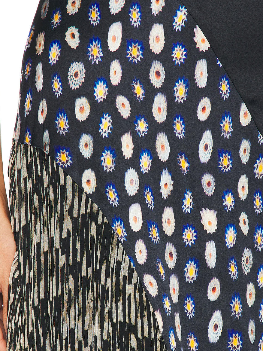 Close-up of the STAUD Fawn Silk Dress in Black Multi, made from stretch silk fabric with multicolored starburst and dot patterns on a dark background, featuring diagonal striped black and white fringe at the lower left corner.