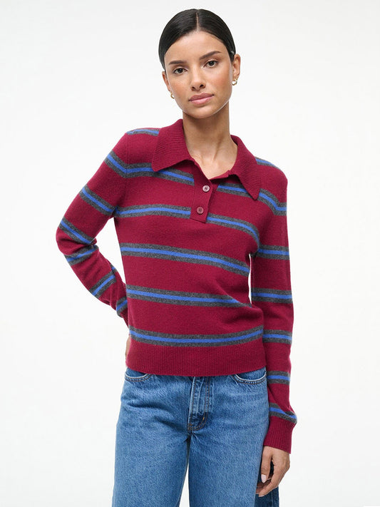 A person stands against a plain background in the STAUD Gemma Cashmere Sweater in Crimson Stripe and blue jeans, with one hand resting on their hip.