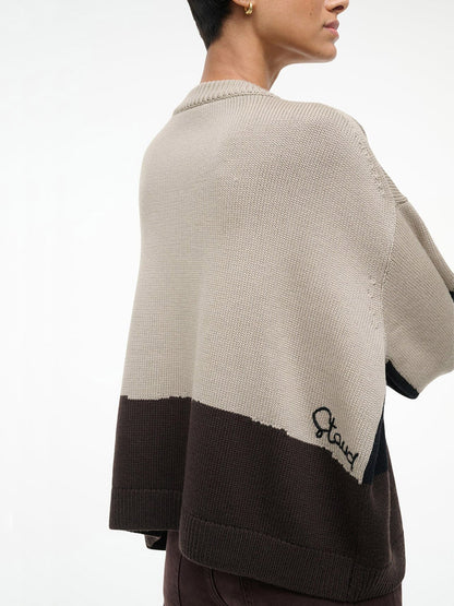 Person wearing the STAUD Giada Sweater in Stables, a color-blocked beige and brown crewneck with "Stand" embroidered near the hem, shown from the back and side. Made from soft merino wool for comfort and style.