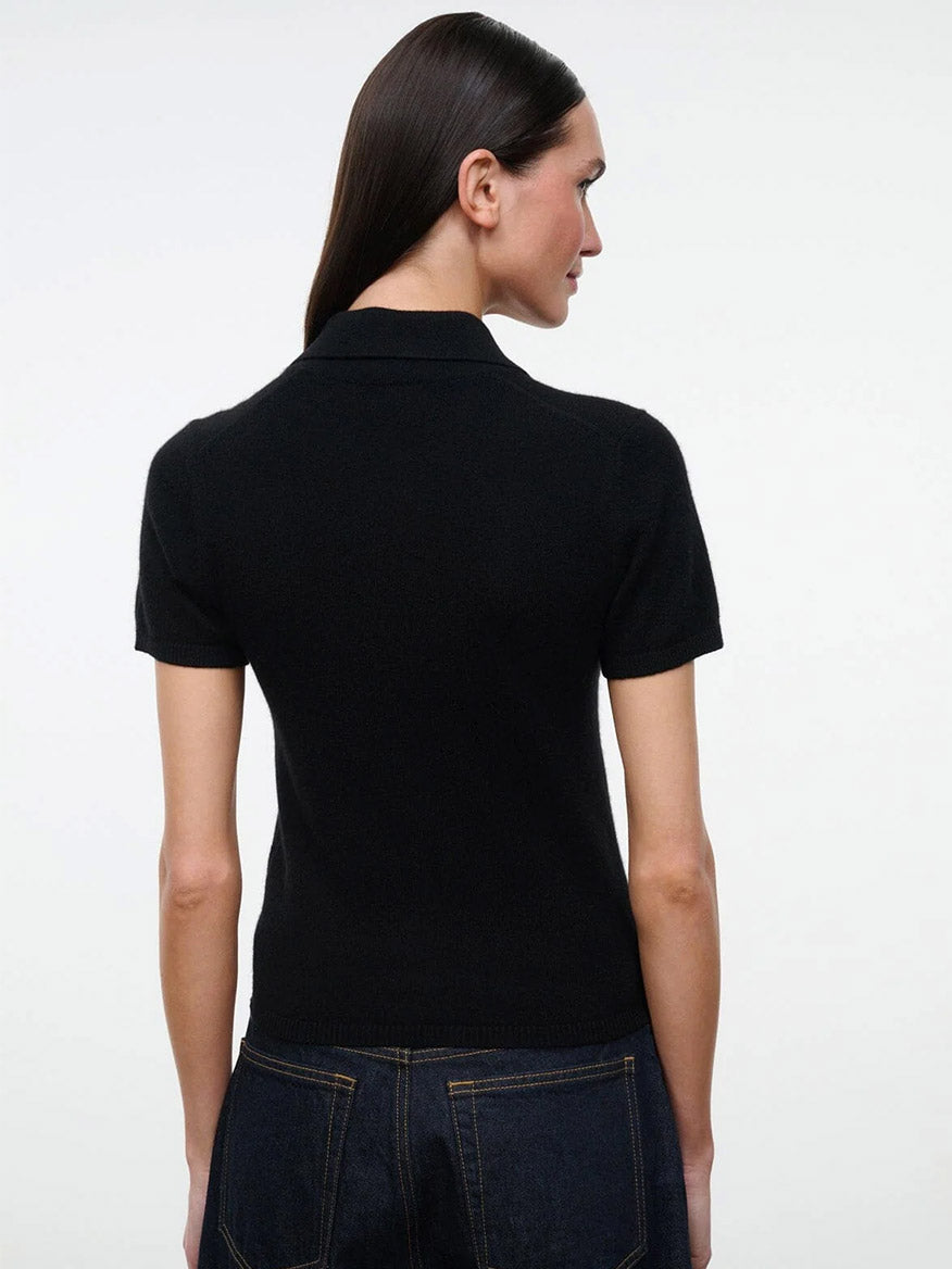 Back view of a person wearing a black STAUD Gino Cashmere Polo Sweater with a fitted, short-sleeved, collared design.