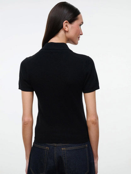 Back view of a person wearing a black STAUD Gino Cashmere Polo Sweater with a fitted, short-sleeved, collared design.