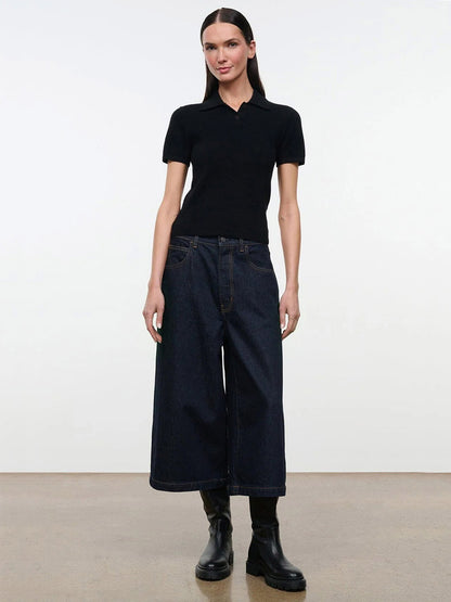 A woman wearing a black STAUD Gino Cashmere Polo Sweater with short sleeves, dark blue wide-leg jeans, and black boots.