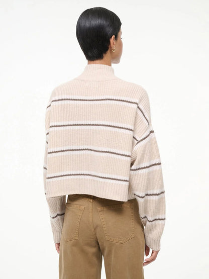 A person with short dark hair is seen from the back against a plain white background, wearing tan pants and the STAUD Hampton Cropped Cashmere Sweater in Whisper Stripe.