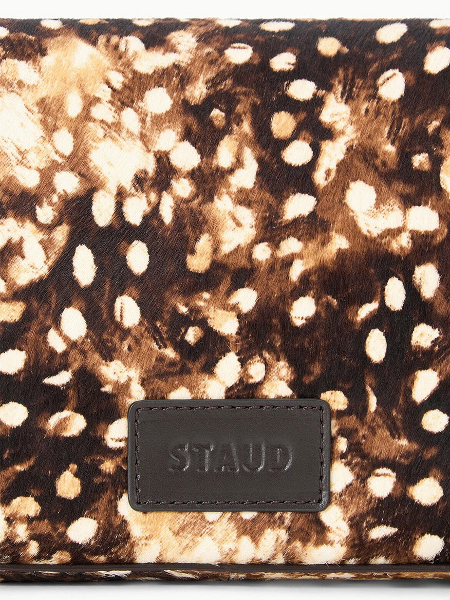 Close-up of a STAUD Harlow Bag in Fawn Haircalf, a brown and white spotted shoulder bag with a leather brand logo patch at the bottom.