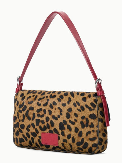 The STAUD Harlow Bag in Cheetah is a rectangular bag featuring an eye-catching cheetah-print haircalf design, accented with a bold red leather shoulder strap, an elegant moon-shaped buckle, and a small red label on the front.
