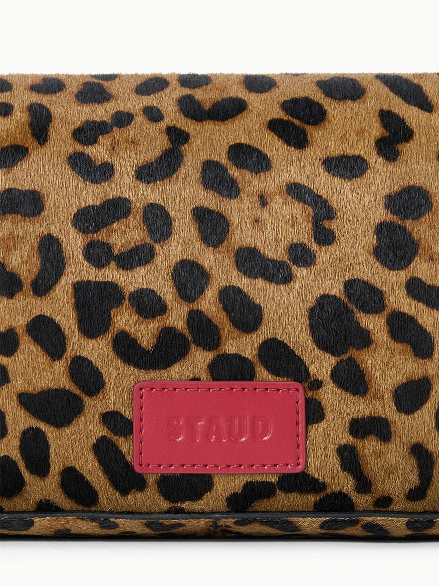 Close-up of the rectangular STAUD Harlow Bag in Cheetah, showcasing a brown and black cheetah-print haircalf pattern with a pink patch labeled “STAUD.”.