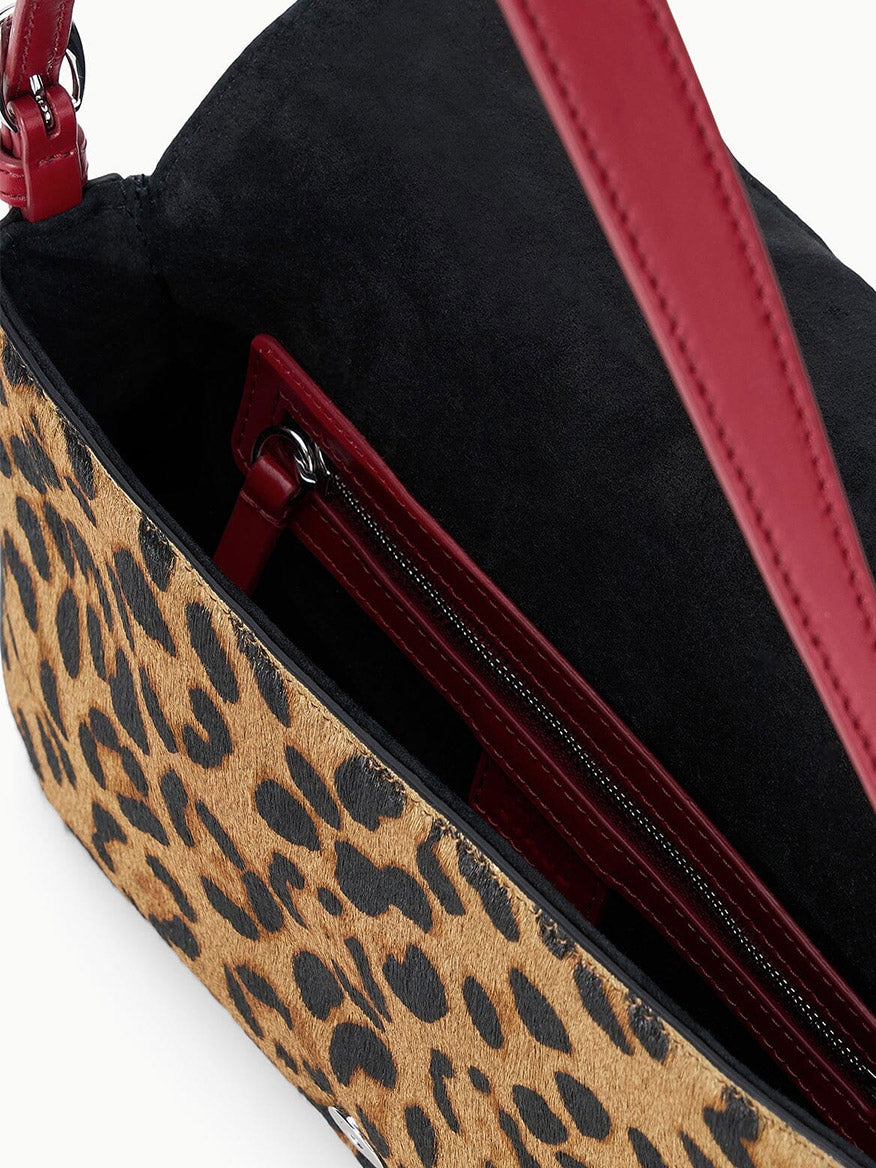 The STAUD Harlow Bag in Cheetah is crafted from luxurious haircalf in a cheetah print, featuring a black interior, striking red strap with a shiny Moon buckle, and an inner zippered pocket.