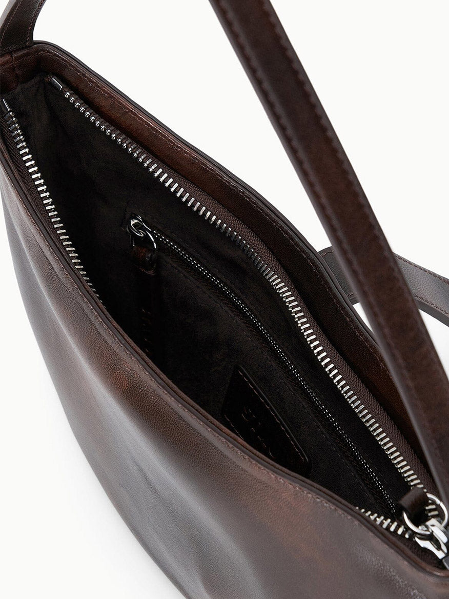 Close-up of the STAUD Harlow Crescent Shoulder Bag in Espresso Distressed leather, featuring a sleek open design that reveals a visible zippered inner pocket and dark fabric lining.
