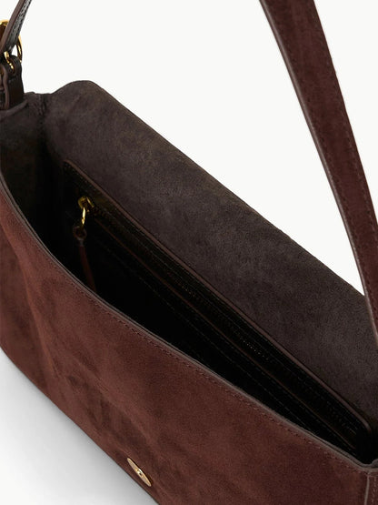 Close-up of the STAUD Harlow Bag in Mahogany Suede, a brown suede shoulder bag with dark interior, inner zippered pocket, and signature moon buckle.