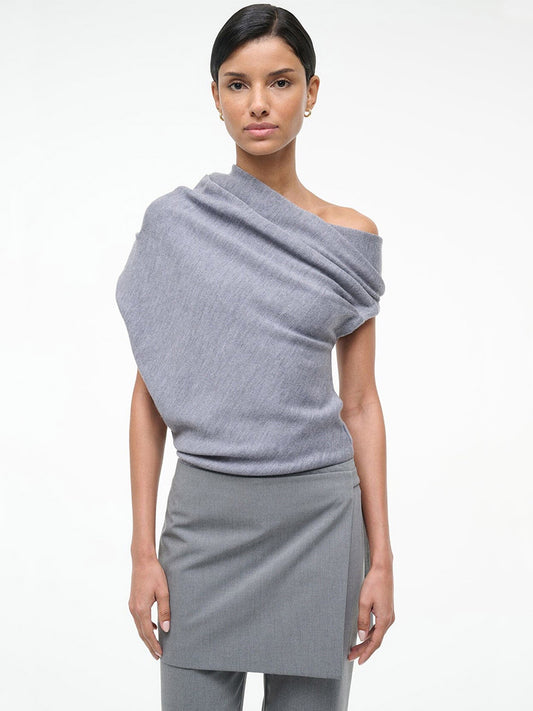 A woman faces forward in a minimal studio, wearing the STAUD Mabel Sweater in Heather Grey with a matching skirt.