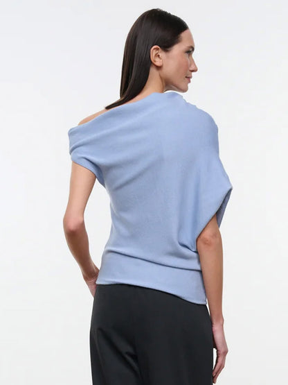 A person wearing a powder blue STAUD Mabel Sweater, an asymmetrical knit top with an off-the-shoulder neckline featuring one cap sleeve and one sleeveless arm.