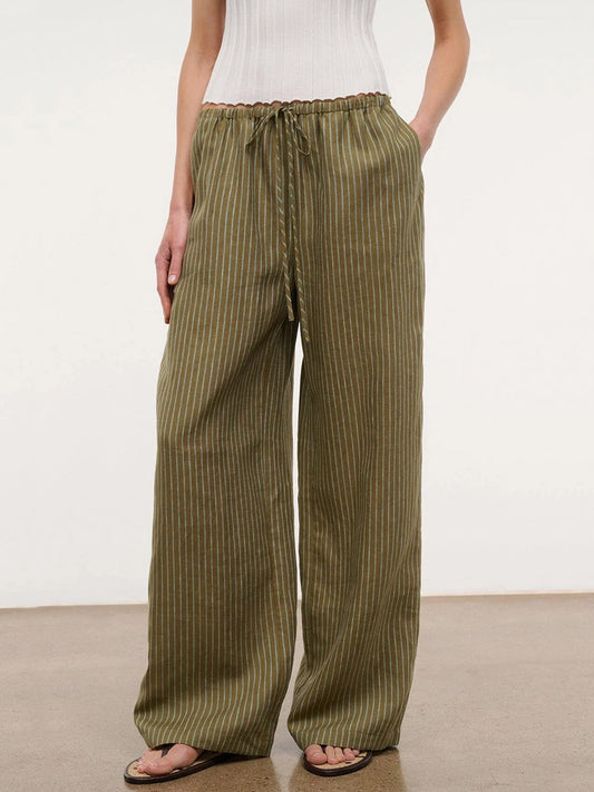 Wearing the STAUD Mateo Linen Pant in Porto Stripe—relaxed fit, wide-leg, drawstring waist—paired with a white sleeveless top and sandals on a brown floor; an ideal look for your warm-weather wardrobe.