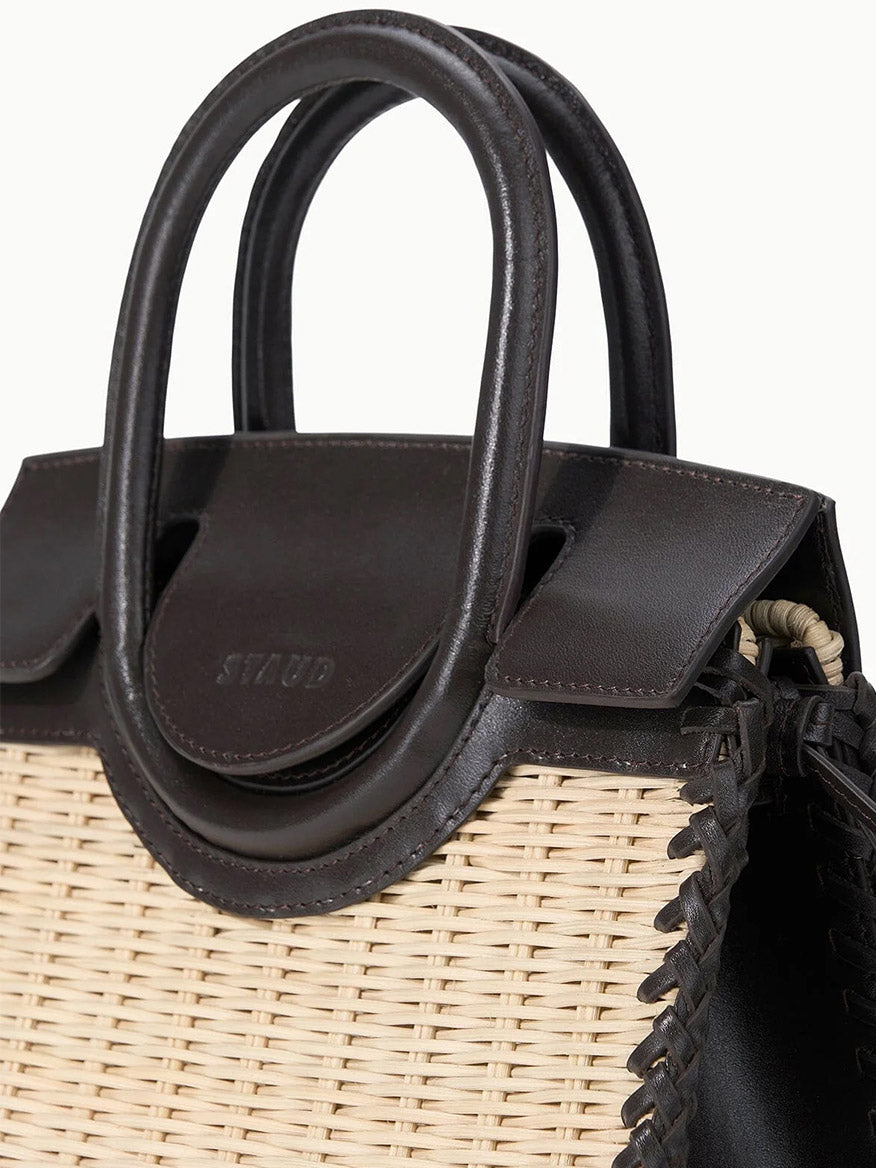 Close-up of the STAUD Maude Mini Wicker Carryall in Natural/Espresso, featuring dark brown leather handles and trim, a woven beige rattan body, crossbody strap option, and visible side stitching.