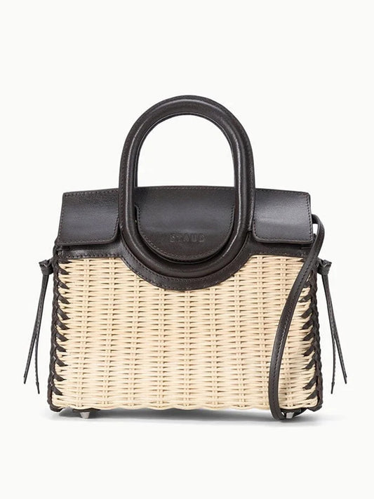 The STAUD Maude Mini Wicker Carryall in Natural/Espresso showcases a structured straw body with a black leather flap and handle, plus a shoulder strap for versatile carrying against any backdrop.
