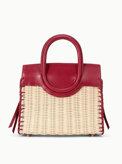 The STAUD Maude Mini Wicker Carryall in Natural/Rouge features a woven straw body with red leather handles and trim, displayed against a plain background.