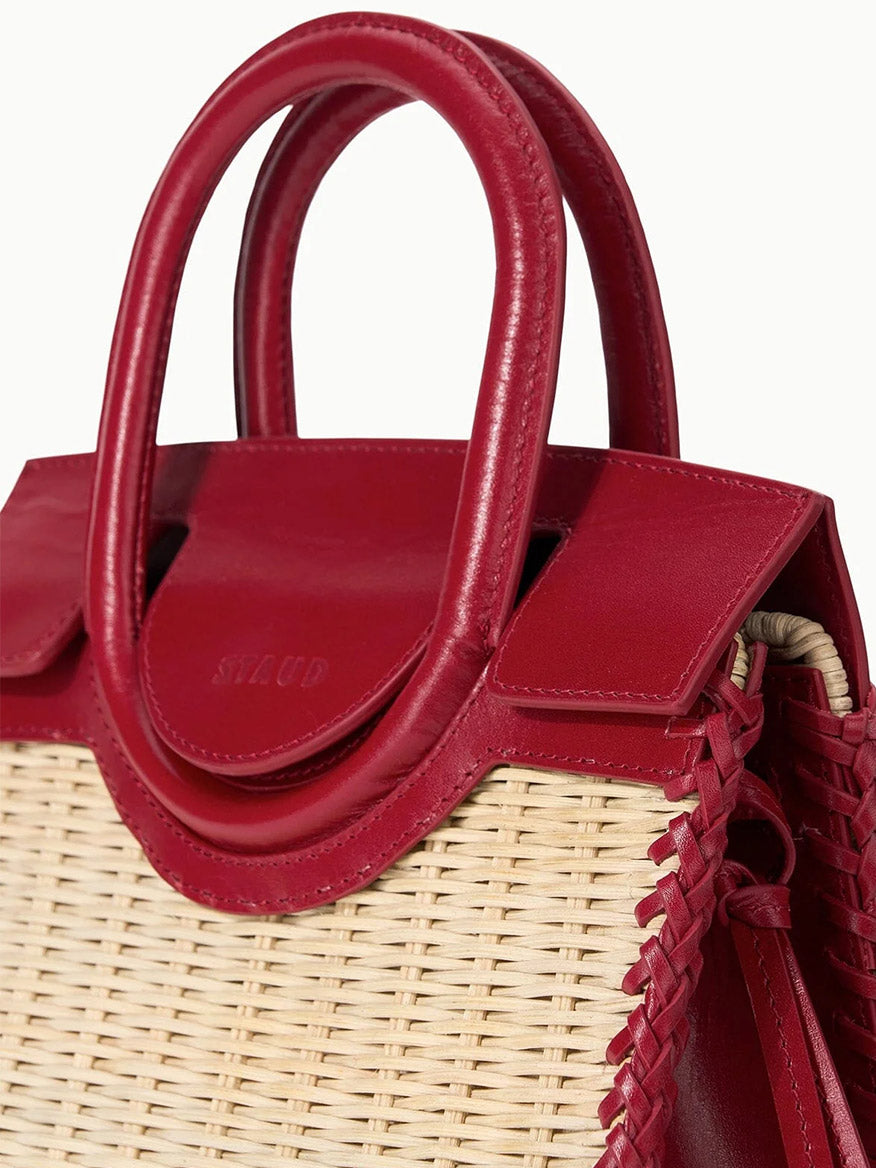 Close-up of the STAUD Maude Mini Wicker Carryall in Natural/Rouge, featuring a woven straw body with red leather handles, trim, and crossbody details.
