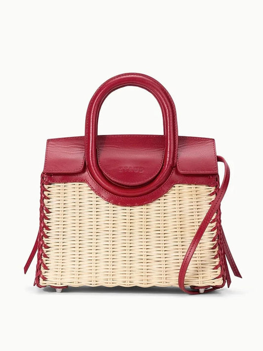 The STAUD Maude Mini Wicker Carryall in Natural/Rouge features a structured wicker base with red leather top, handles, and trim, plus a crossbody strap, shown against a white background.