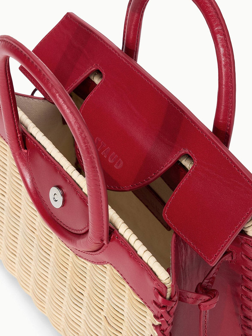 A close-up of the STAUD Maude Mini Wicker Carryall in Natural/Rouge, featuring red leather handles and trim, a magnetic snap closure, and visible stitching.