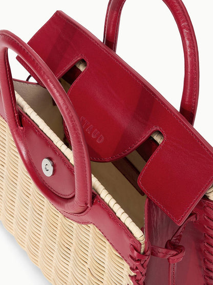 A close-up of the STAUD Maude Mini Wicker Carryall in Natural/Rouge, featuring red leather handles and trim, a magnetic snap closure, and visible stitching.