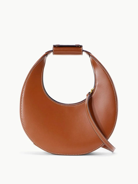 The STAUD Mini Moon Tote Bag in Tan features a crescent moon shape with a short handle and a sleek crossbody strap.