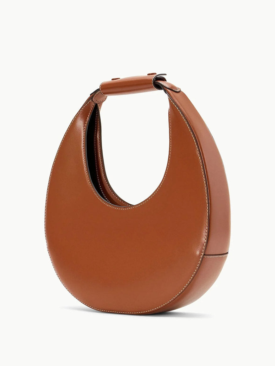 STAUD Moon Tote Bag in Tan, crafted in brown leather with a unique crescent moon shape, features visible stitching along the edges and an indulgent suede lining.