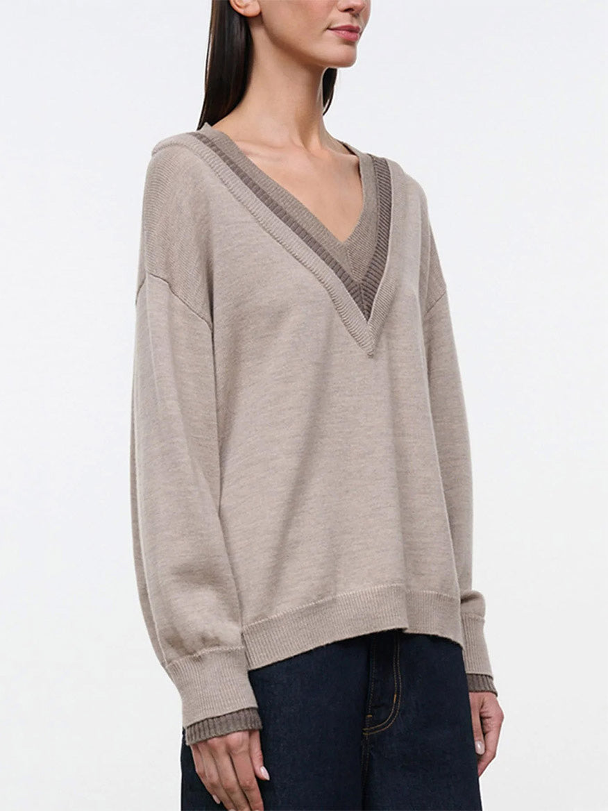 The STAUD Norman Sweater in Sesame Multi is an oversized, tan V-neck sweater featuring a contrasting ribbed hood and a triple-layer neckline.