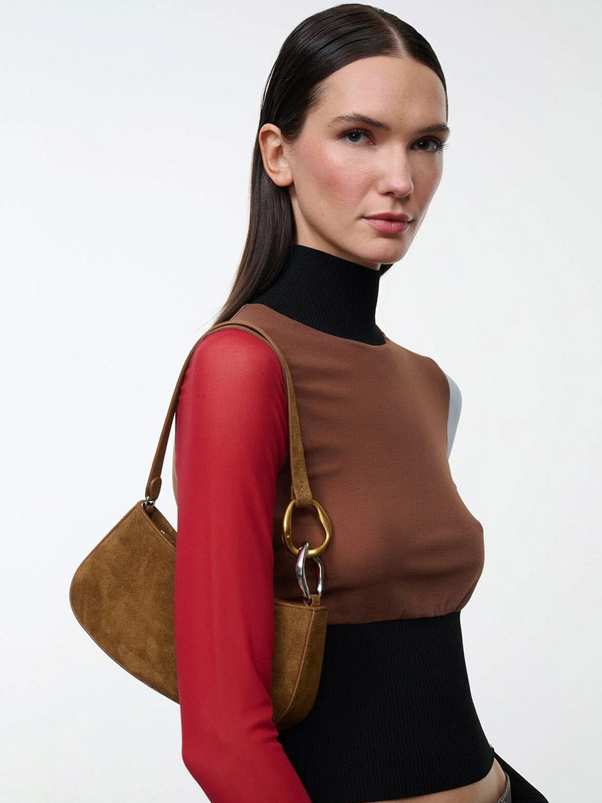 A model wearing a compact brown suede STAUD Ollie Bag in Cigar, featuring a gold and silver ring accent on the strap.