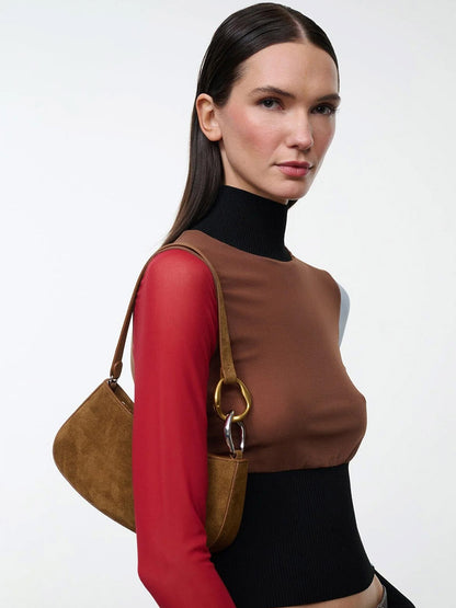A model wearing a compact brown suede STAUD Ollie Bag in Cigar, featuring a gold and silver ring accent on the strap.