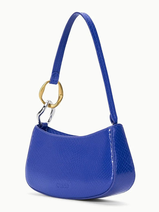 The STAUD Ollie Bag in Cobalt is a small blue snake-print leather mini shoulder bag with a short strap and large gold ring detail, shown against a plain white background.
