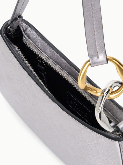 Close-up of the STAUD Ollie Bag in Pewter, a metallic silver mini shoulder bag with a zipper closure, black interior, and two-tone gold and silver ring hardware on the strap.