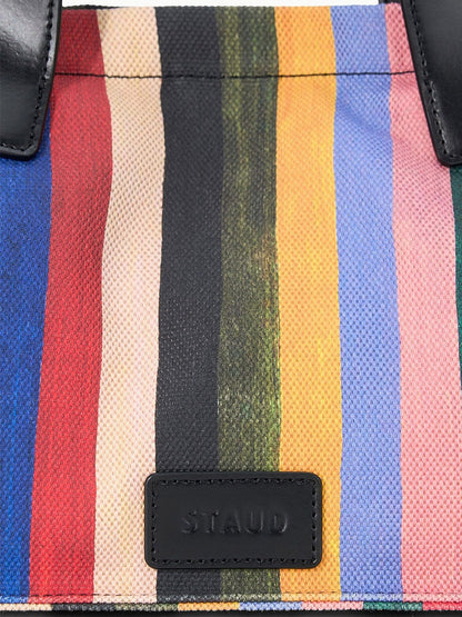 A close-up of the STAUD Port Tote in Artist Stripe, featuring vertical multicolored stripes, a black leather "STAUD" patch, and sturdy leather handles for a chic look.