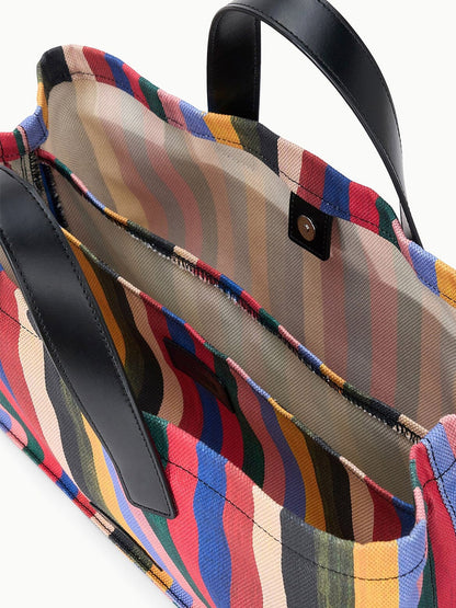 STAUD Port Tote in Artist Stripe features an open structure with black leather handles, a multicolored striped fabric interior, an interior zip pocket, and a snap closure.