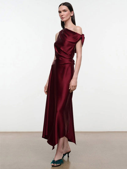 A model wearing the STAUD Portia Silk Dress in Carmino, an asymmetrical burgundy midi dress with a draped bodice and gathered waist with adjustable ties.