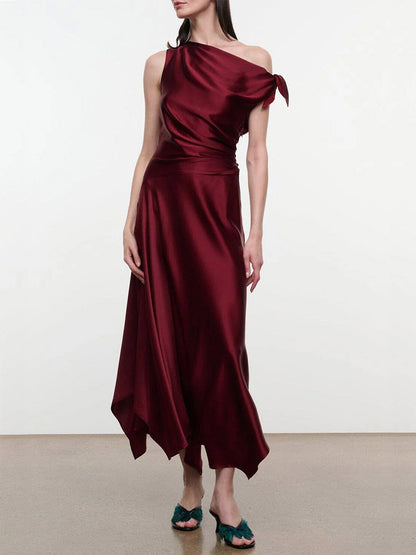 STAUD Portia Silk Dress in Carmino featuring a one-shoulder draped bodice and handkerchief hem, styled with dark green feathered heels.