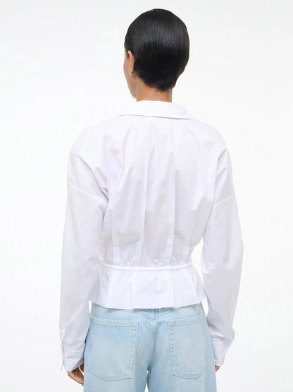 Individual with short dark hair, seen from the back against a white background, wearing the STAUD Primrose Shirt in White paired with light blue jeans.
