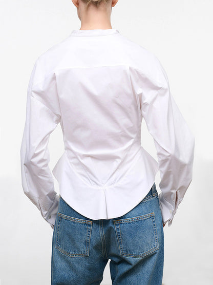 A person is shown from the back against a plain white background, wearing the STAUD Rhys Stretch Top in White—a long-sleeve, band-collar shirt with a curved hemline—paired with blue jeans.
