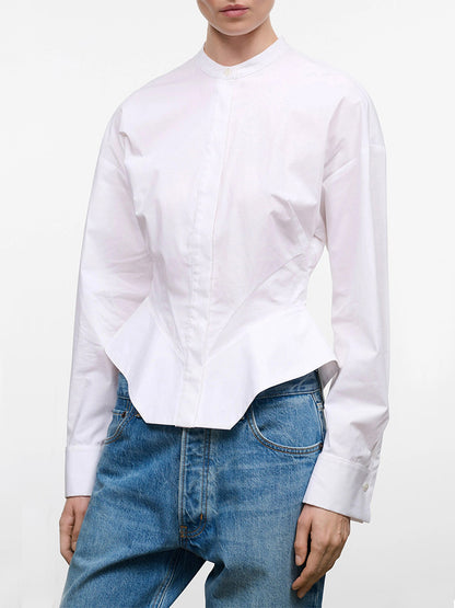 A person wearing the STAUD Rhys Stretch Top in White, a structured long-sleeve band-collar shirt with barrel cuffs and a fitted waist, paired with blue jeans, shown from shoulders to hips against a plain background.
