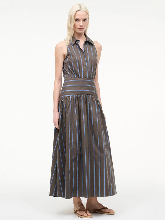 A woman wears the STAUD Romy Dress in Huntington Stripe—a sleeveless, collared, button-up maxi dress with vertical brown and blue stripes and a wide striped waistband, styled with sandals.