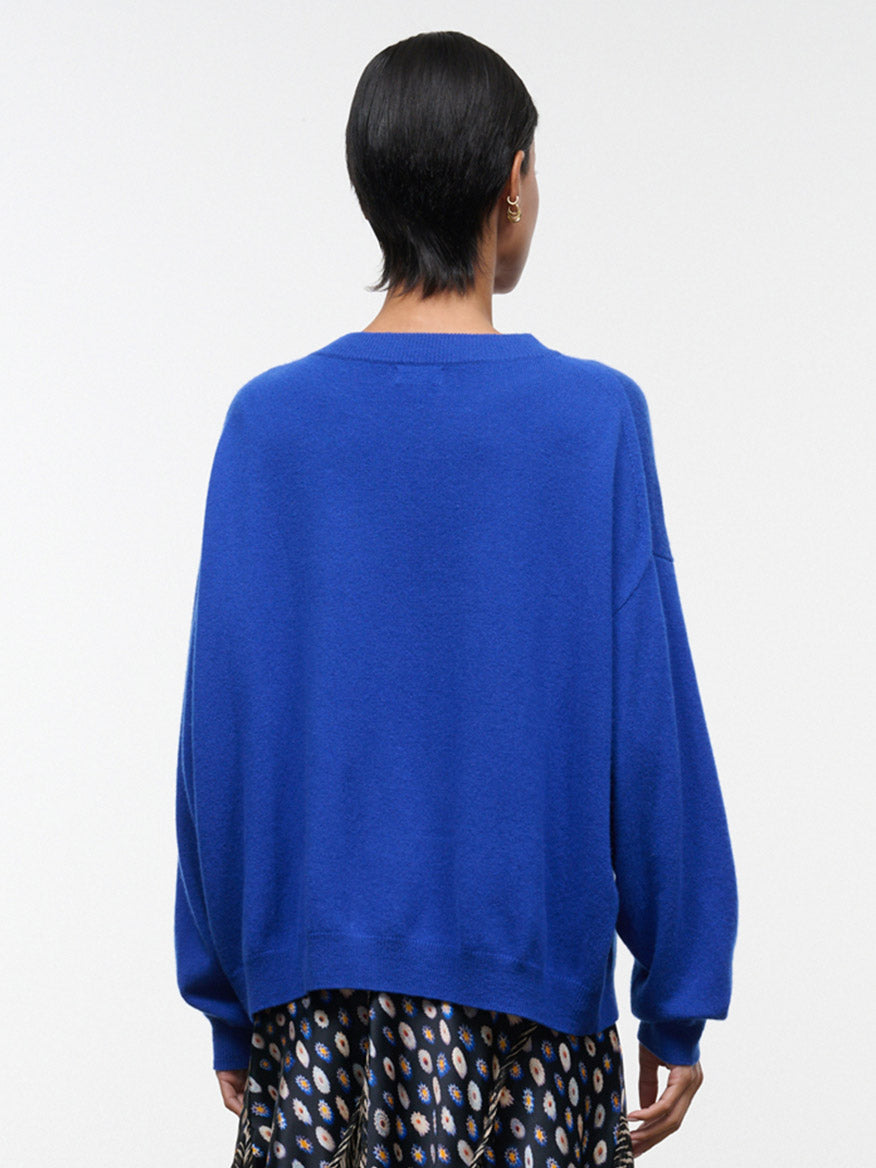 A person with short dark hair is shown from the back against a plain white background, wearing the STAUD Spencer Cashmere Sweater in Cobalt styled with a patterned skirt.
