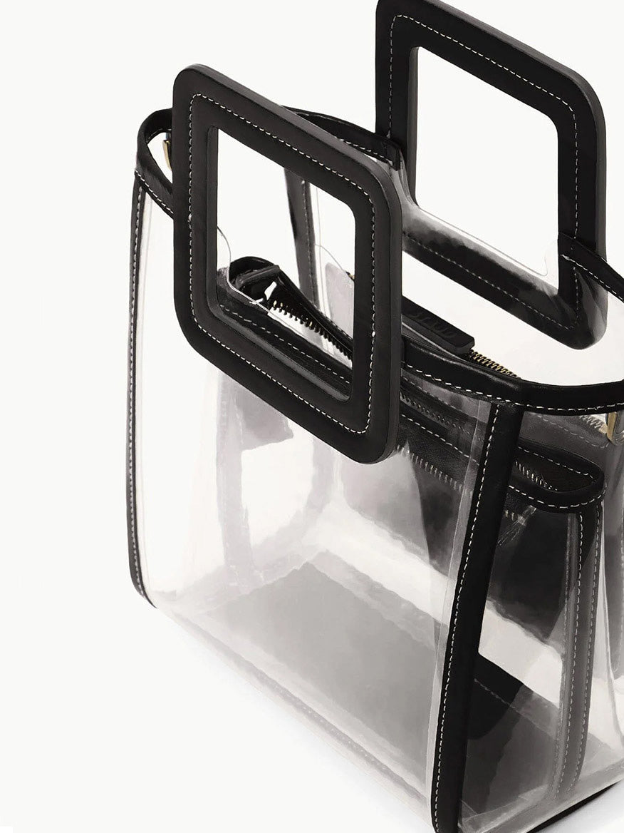 The STAUD Stadium Mini Shirley Bag in Clear/Black features clear PVC, black trim, square handles, and white stitching with a visible inner zip pouch—stylish, stadium-approved, and perfect for events.