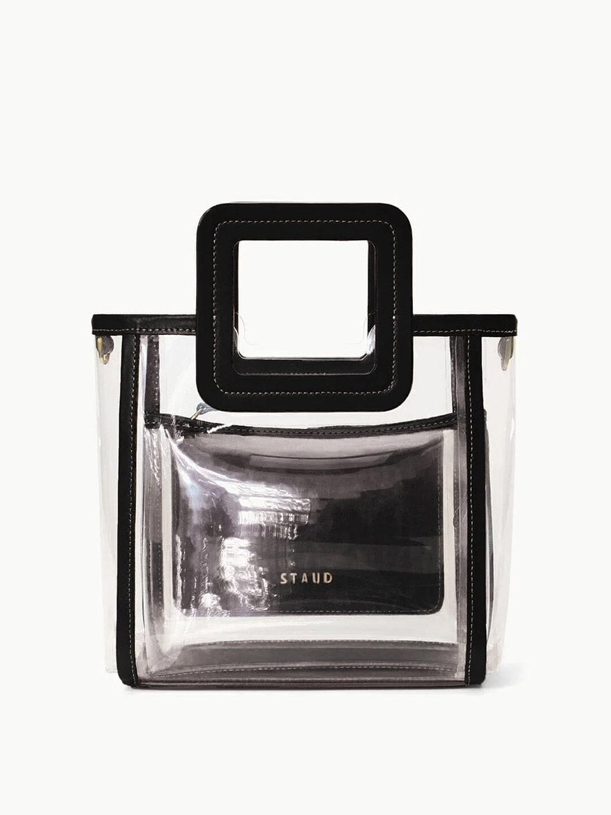 The STAUD Stadium Mini Shirley Bag in Clear/Black features a clear PVC body, black trim, square handle, and an inner clear pouch with "STAUD" in gold—stylish and perfect for stadium events.