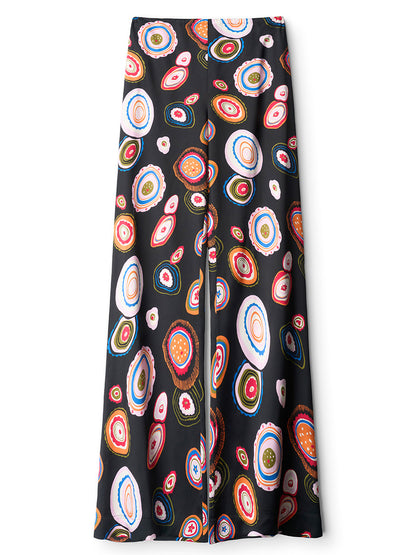 The STAUD Stroll Silk Pant in Millefiore 2.0 is a black straight-leg pant adorned with a repeating print of vibrant, circular abstract motifs, crafted from stretch silk satin and finished with an elastic waistband for extra comfort.