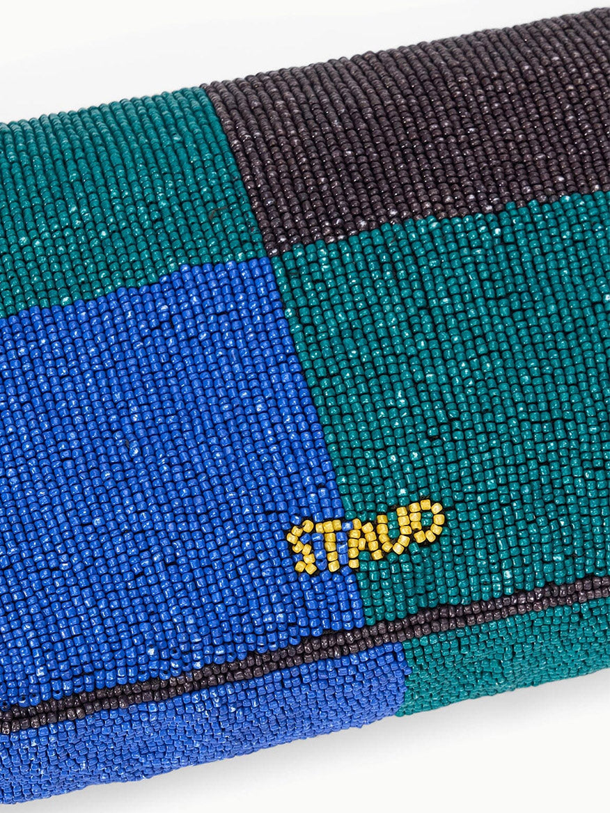 The STAUD Timmy Shoulder Bag in Conch Shell features blue, green, and black beaded sections spelling "STAND" in yellow beads and has a magnetic closure for easy access.