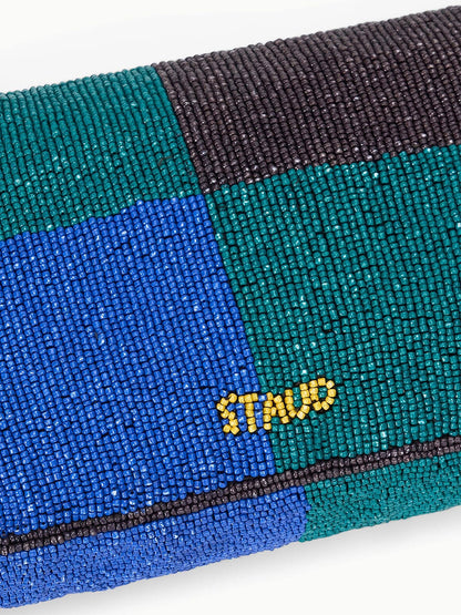 The STAUD Timmy Shoulder Bag in Conch Shell features blue, green, and black beaded sections spelling "STAND" in yellow beads and has a magnetic closure for easy access.