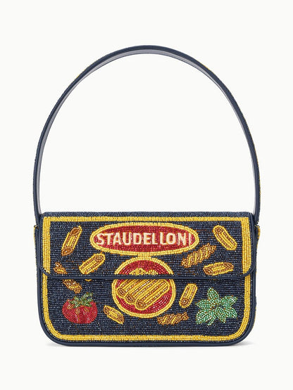 The STAUD Tommy Beaded Bag in Staudelloni is a limited-edition shoulder bag with a navy strap, decorated with yellow pasta shapes, a tomato, basil leaf, and “STAUDELLONI” in red and yellow on the front flap.