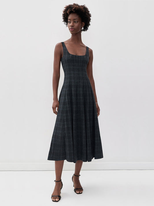 A model wearing the STAUD Wells Midi Sleeveless Dress in Ink Blue Plaid, a navy blue midi-length corset-style dress with a square neckline, a fitted waist, and a full skirt.