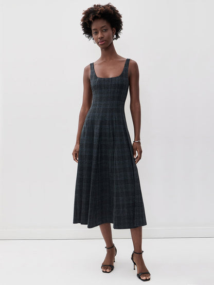 A person wears a STAUD Wells Midi Sleeveless Dress in Ink Blue Plaid, featuring a square neckline, fitted waist, and a full skirt.