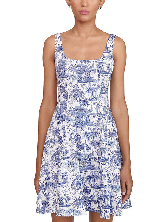 A woman wears the STAUD Wells Mini Sleeveless Dress in China Blue Toile, featuring a white cotton poplin fabric, square neckline, blue toile pattern, and flared skirt, standing against a plain background.