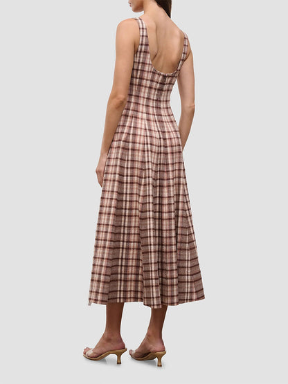 A woman stands facing away, wearing the STAUD Wells Sleeveless Dress in Tuscany Plaid with heeled sandals.
