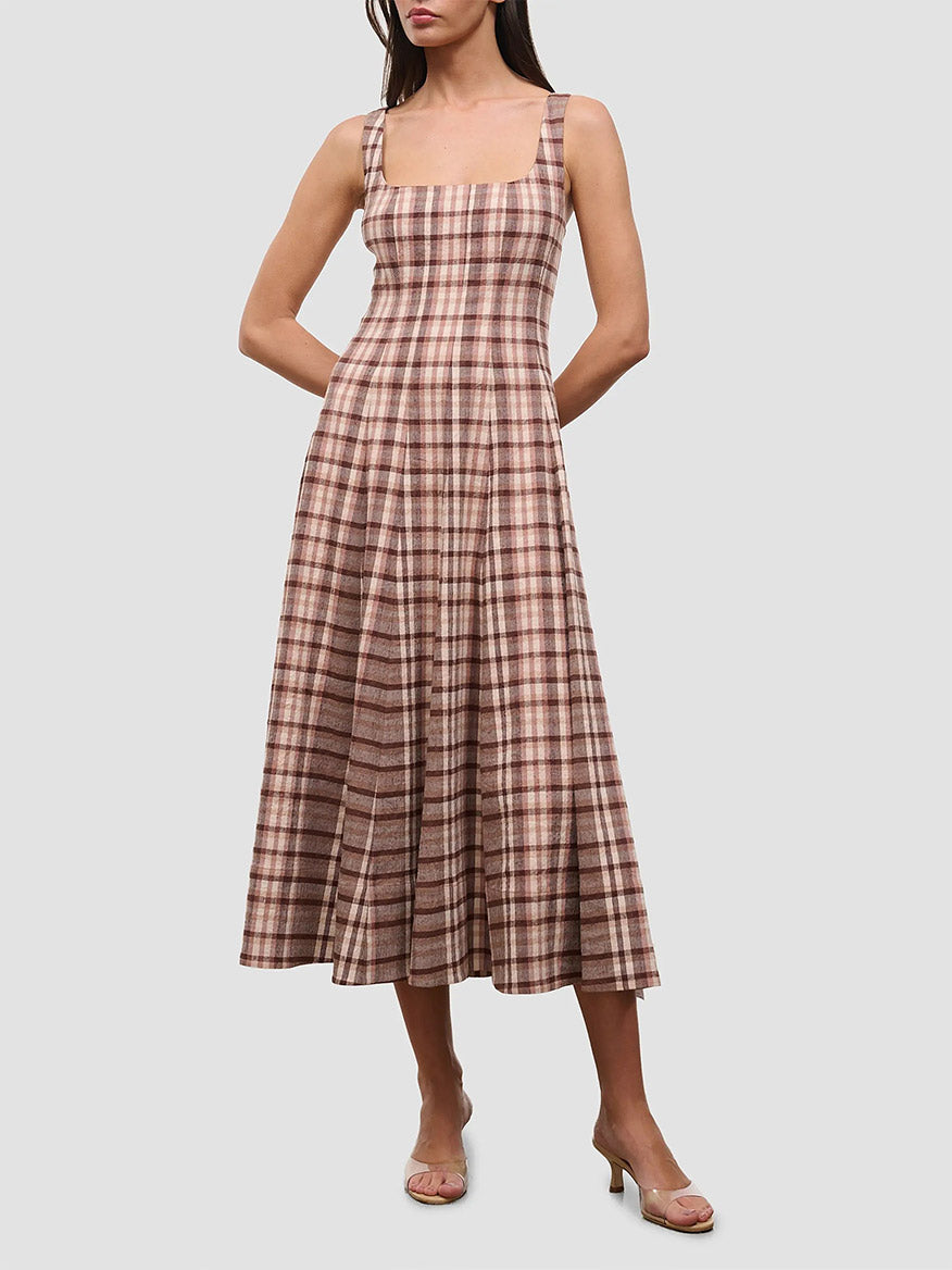 A woman is wearing the STAUD Wells Sleeveless Dress in Tuscany Plaid, an ankle-length cotton poplin dress featuring a fitted bodice and square neckline, paired with clear-heeled sandals and standing against a plain background.